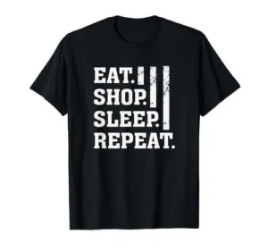 A black crew neck t-shirt featuring bold white screen print text that reads eat shop sleep repeat.