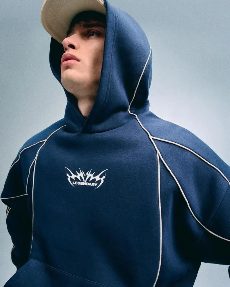 A close-up shot of a young man wearing a navy blue hoodie featuring thin white contrast reflective piping along the seams and a sharp white legendary screen print logo on the chest